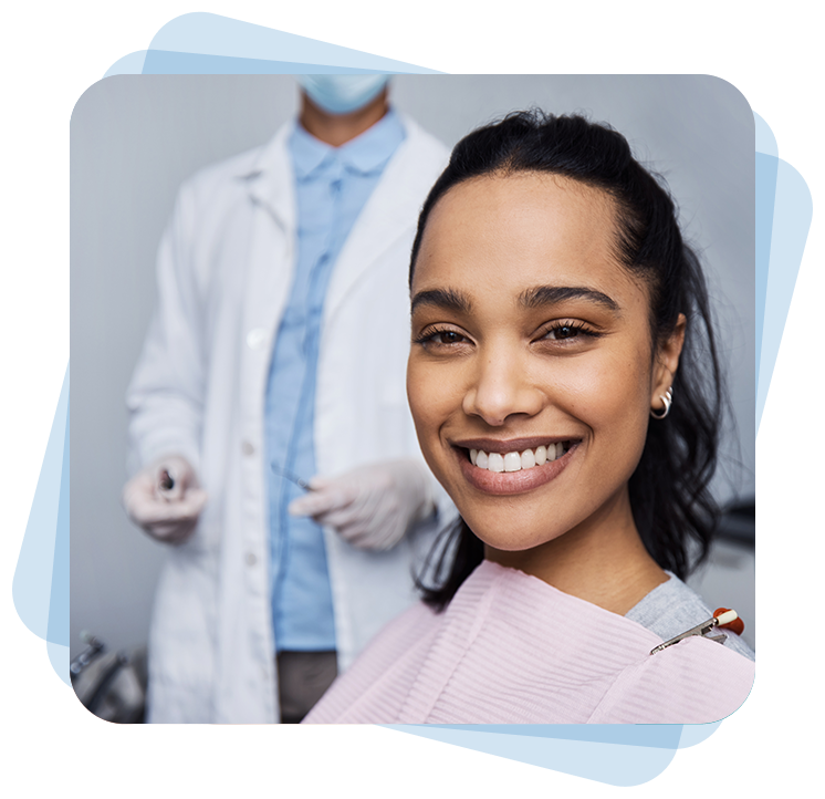 A woman smiles at the camera in a dental office, wearing a bib. A dentist in a white coat and gloves stands in the background holding dental tools.