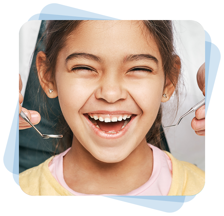 A child smiles broadly, seated in a dental chair, with dental tools held near her mouth by a dentist.